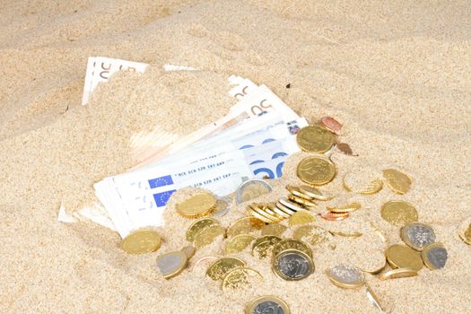 Euro bank notes and coins in the sand