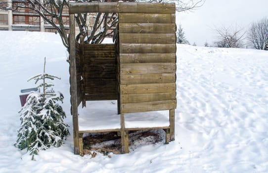 beach changing booth full of snow and next to a small tree in cold winter time