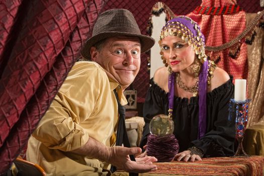 Fortune teller in head scarf with skeptical customer and crystal ball