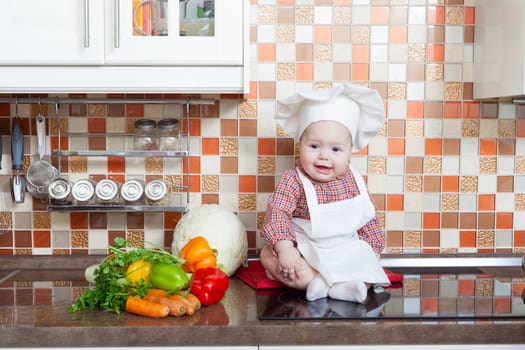 Baby cook with vegetables sits on a kitchen table