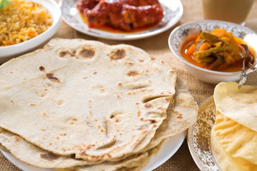 Chapatti roti or chapati, curry chicken, biryani rice, salad, masala milk tea and papadom. Indian food on dining table. 