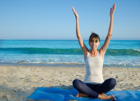 Young pretty woman practicing yoga on the beach by the ocean 