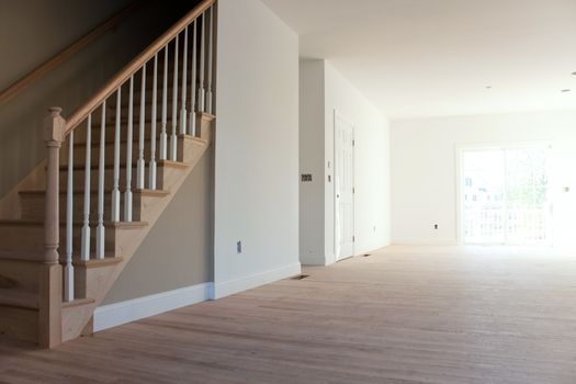 New home construction interior room with unfinished wood floors stairway and railings. Electrical and hvac connections also are partially unfinished.