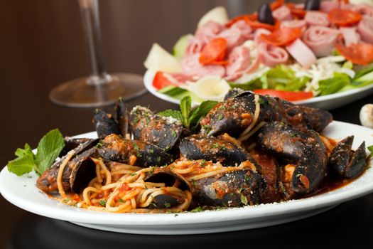 Mussels dinner with red sauce and pasta and an antipasto salad.  Shallow depth of field.