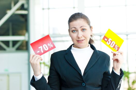 Brunette girl in confusion holds two tablets with discounts