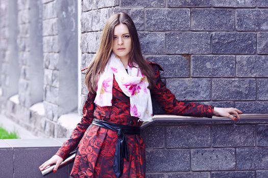 Beautiful girl in a red cloak against a brick wall