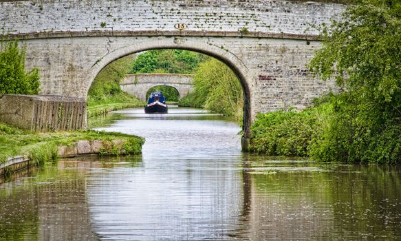 A narrowboat sailing on the Shropshire Union Canal between two bridges