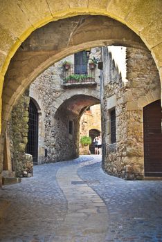 Looking uphill through a medieval arch at a pretty cobbled street in Pals, Spain