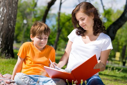 boy and a woman in a summer park reading a book together