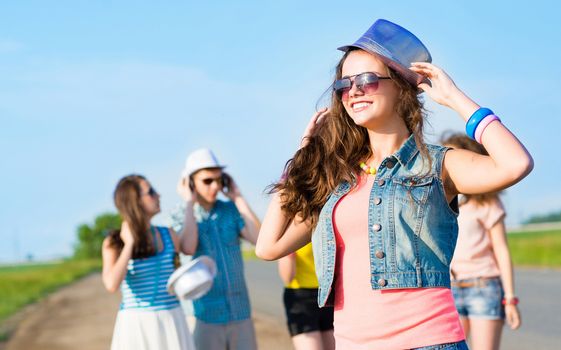 stylish young woman in sunglasses on the background of blue sky and friends