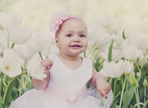 Little girl in an elegant dress to stand near blossoming tulips