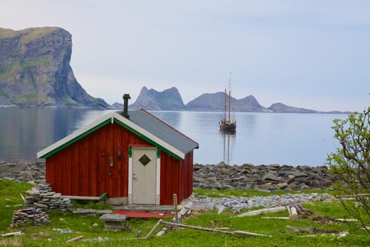 Old fishing hut in scenic fjord with sailing ship in Norway