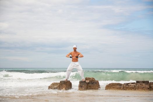 healthy man doing pilates yoga meditation on beach summer freedom