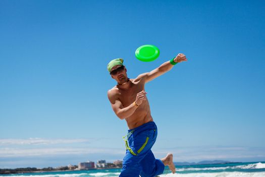 attractive man playing frisby on beach in summer sport fitness jump