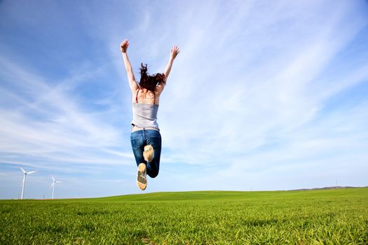 Young beautiful woman jumping for joy on green sunny field