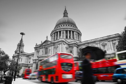 St Paul's Cathedral in London, the UK. Red buses in motion and man walking with umbrella.