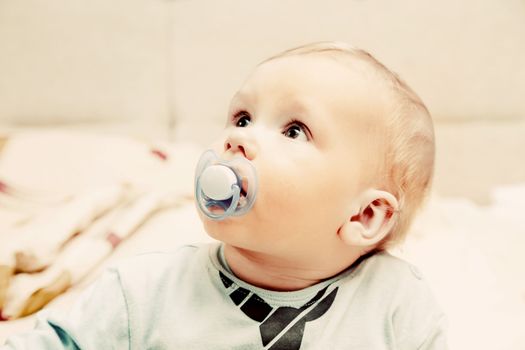 Young baby boy with a dummy in his mouth looking above