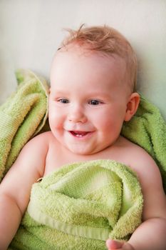 A happy smiling baby lying on bed in green towel