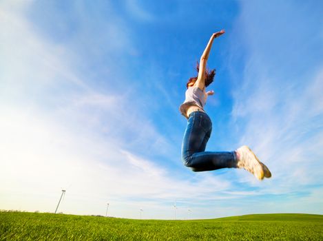 Young beautiful woman jumping for joy on green sunny field