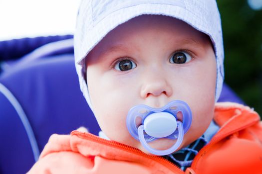 Young baby boy with a dummy in his mouth. Outdoors portrait