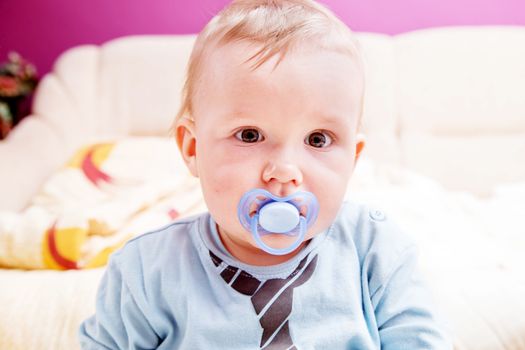 Young baby boy with a dummy in his mouth looking at the camera