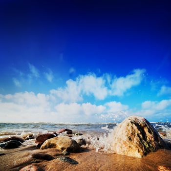 Waves hiting rocks on the beautiful natural beach. Blue sunny sky