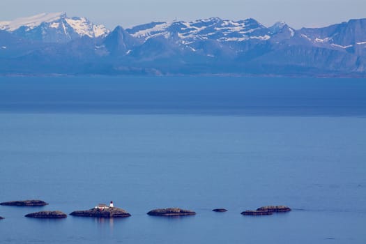 Lighthouse on tiny rocky islets near Lofoten islands with mountainous norwegian coast in the background