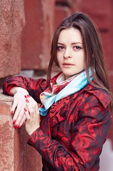 Beautiful girl in a red cloak against a brick wall