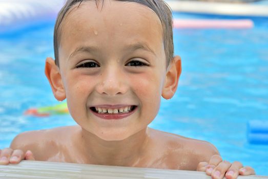 A happy six year old boy enjoys his summertime in the pool.