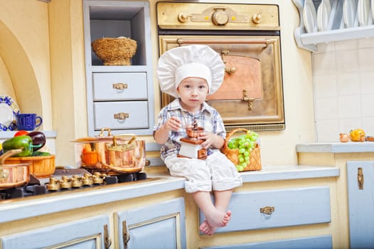little boy sits on a kitchen table and plays the cook