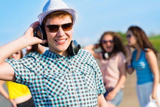 young man in sunglasses, headphones holds a hand on a background of blue sky and friends