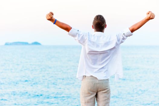 man with hands raised at the beach