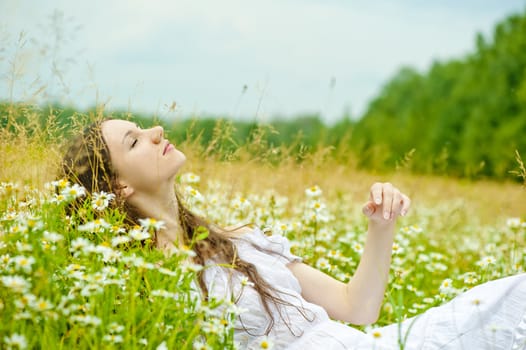 girl in a white sundress lies in camomile field