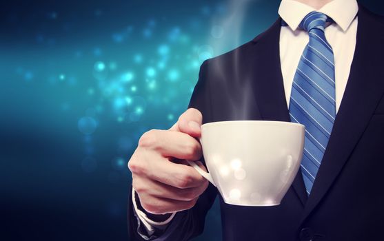 Business man holding a steaming cup of hot coffee on blue modern background