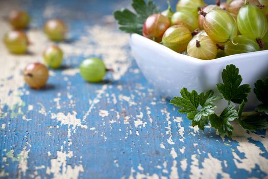 Gooseberries in bowl with leaves on old table background, copy space