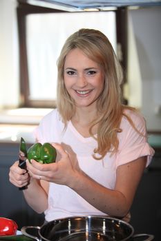 Beautiful young blond woman preparing vegetables in the kitchen cutting a green bell pepper with a knife