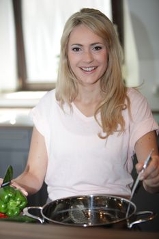 Smiling woman cooking in the kitchen standing over a stainless steel pot on the stove stirring the contents