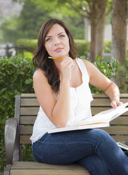 Attractive Young Adult Female Student on Bench Outdoors with Books and Pencil.