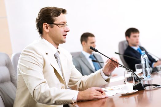 Portrait of a businessman, said into the microphone, in the background colleagues communicate with each other