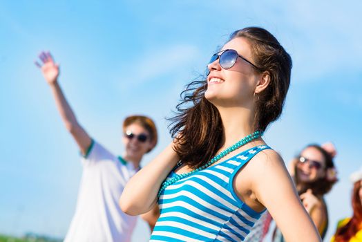 stylish young woman in sunglasses on the background of blue sky and friends