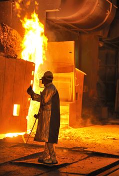 A steel worker takes a sample from oven