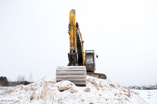 earthmover excavator stand on quarry pile sand pit soil earth covered with snow in winter. heavy construction industry.