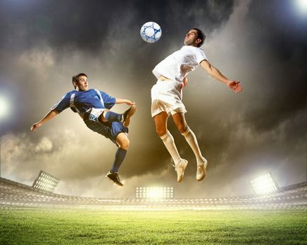 two football players in jump to strike the ball at the stadium