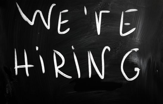 "We are hiring!" handwritten with white chalk on a blackboard