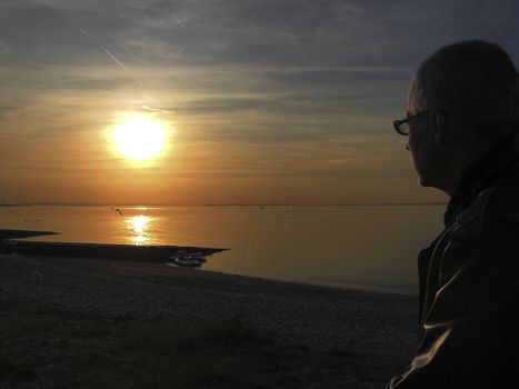 Male looking into the sun setting over a calm sea
