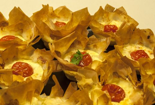 Small homemade pies with cheese and cherry tomato in a basket of pastry