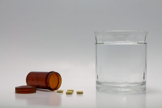 Pills spilling from bottle and a glass of water.