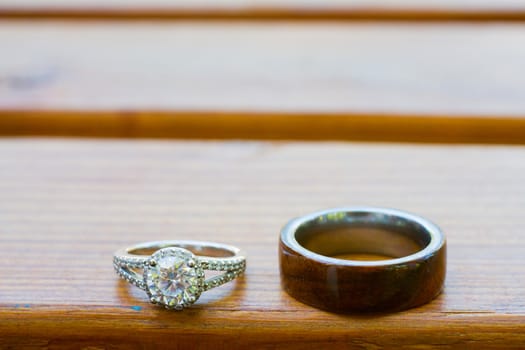 The rings of a bride and groom are photographed on a wooden bench.