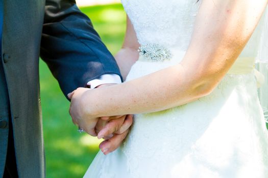 This bride and groom hold hands romantically while kissing on their wedding day.