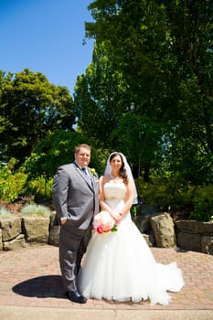 A beautiful bride and groom pose for portraits on their wedding day at a park outdoors.